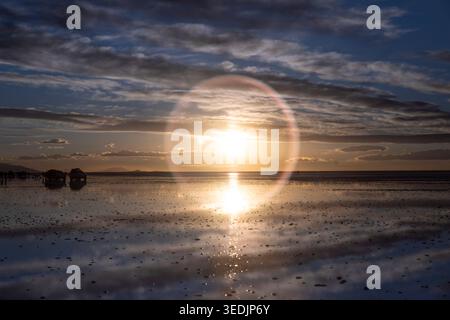 Die untergehende Sonne erzeugt einen spektakulären Rundlichtfleck über der überfluteten Oberfläche des Salar de Uyuni, der größten Salzfläche der Welt in i Stockfoto