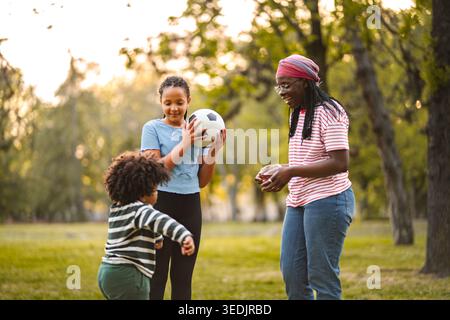 Familie spielt zusammen Fußball im Park bei Sonnenuntergang Stockfoto