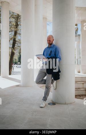 Geschäftsmann liest Dokumente, während er sich an die Marmorsäule am modernen Säuleneingang lehnt Stockfoto