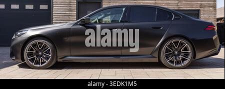 Slowenien, Ljubljana - 8. April 2026: Der BMW M5 parkt an einem sonnigen Tag vor einer Holzkonstruktion. Stockfoto