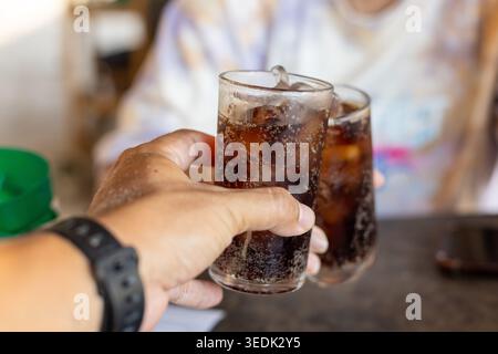 Nahaufnahme: Die Person hält ein Glas mit kaltem, erfrischendem Limonade und Eis, das während der fröhlichen Feier beim Genuss eines süßen Getränks Toast macht Stockfoto