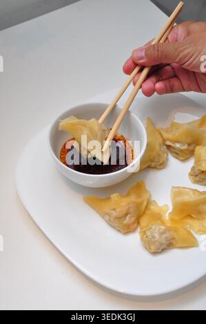 Gedämpftes Wonton mit Chili-Öl-Dip serviert auf einem weißen Teller auf dem weißen Tisch Stockfoto