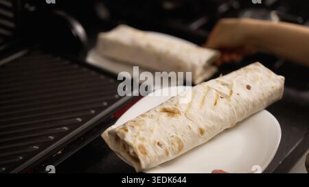 Nahaufnahme von Händen, die eine frisch zubereitete Shawarma oder Burrito in eine Papierserviette wickeln. Köstliches hausgemachtes Fast Food wird zum Servieren zubereitet. Eine Platte mit cu Stockfoto