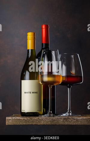 Gläser Rot- und Weißwein mit Flaschen auf dunklem Hintergrund Stockfoto