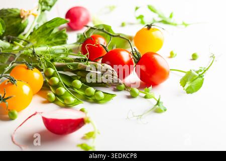 Frische grüne Erbsenschoten mit Sprossen, Rettich, Tomaten und grünem Spargel auf weißem hölzernem Hintergrund. Konzept der gesunden Ernährung, frisches Gemüse. Stockfoto