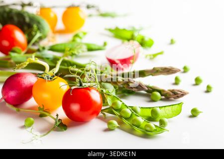 Frische grüne Erbsenschoten mit Sprossen, Rettich, Tomaten und grünem Spargel auf weißem hölzernem Hintergrund. Konzept der gesunden Ernährung, frisches Gemüse. Stockfoto