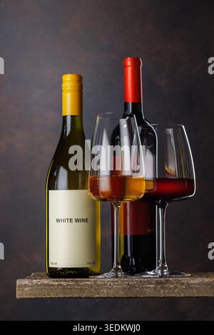 Gläser Rot- und Weißwein mit Flaschen auf dunklem Hintergrund Stockfoto