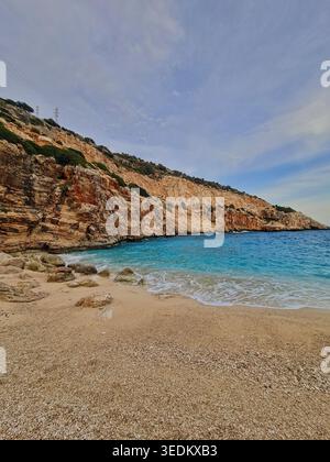 Malerische mediterrane Bucht mit türkisfarbenem Wasser, Sandstrand mit Kieselsteinen, zerklüfteten Kalksteinfelsen, sanften Wellen und einem sanften blauen Himmel an einer ruhigen Küste Stockfoto