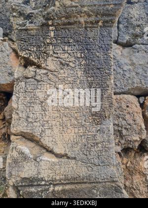 Verwitterte antike Steinplatte mit geschnitztem griechischen Text, die zwischen archäologischen Ruinen als historisches epigraphisches Artefakt erhalten wurde. Stockfoto