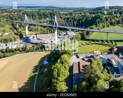 Aus der Vogelperspektive auf die Poya-Brücke, die ein üppiges grünes Tal mit Industriebauten und sanften Hügeln unter einem klaren Himmel überspannt Fribourg, Freiburg, Schweiz Stockfoto