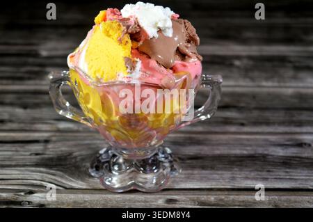 Ein Eisbecher mit verschiedenen Geschmacksrichtungen, der in einem Glasbecher im Vintage-Stil serviert wird, bietet mehrere Kugeln mit verschiedenen Eissorten, wie Schokolade, St. Stockfoto