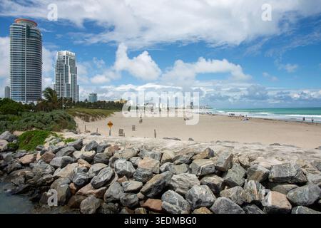 Felsiger Wellenbrecher und Sandstrand mit modernen Stadtgebäuden, die hinter ihnen in South Beach, Miami, aufragen. Eine markante Küstenzusammensetzung. Stockfoto
