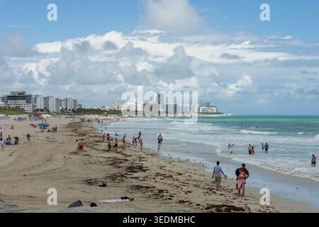 Menschenmassen genießen einen Tag am Strand mit der Skyline von Miami und den Meereswellen im Hintergrund. Eine lebhafte und ikonische Szene in South Beach. Stockfoto