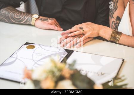 Die Hände eines frisch verheirateten Paares werden über ihre Heiratsurkunde zusammengelegt, was ihre vereinigung symbolisiert Stockfoto