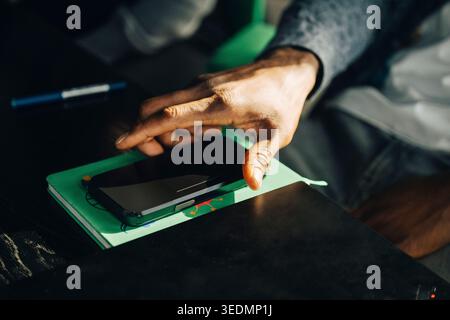 Nahaufnahme eines Geschäftsmannes, der sein Smartphone vom Schreibtisch im Büro abholte Stockfoto