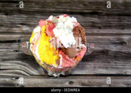 Ein Eisbecher mit verschiedenen Geschmacksrichtungen, der in einem Glasbecher im Vintage-Stil serviert wird, bietet mehrere Kugeln mit verschiedenen Eissorten, wie Schokolade, St. Stockfoto