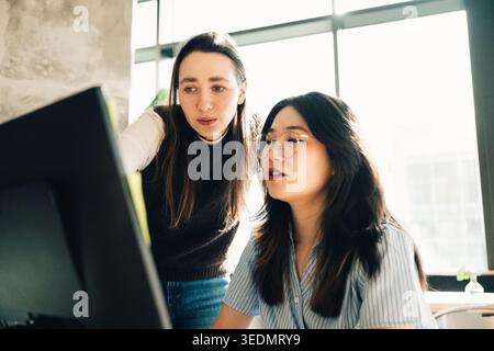Weibliche Kollegen diskutieren über Projekte, während sie im Büro am Computer arbeiten Stockfoto