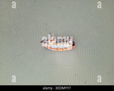 Aus der Vogelperspektive auf ein rostiges verlassenes Fischerboot, das in ruhigem, trübem Wasser mit verwittertem Rumpf und Deck schwimmt. Stockfoto