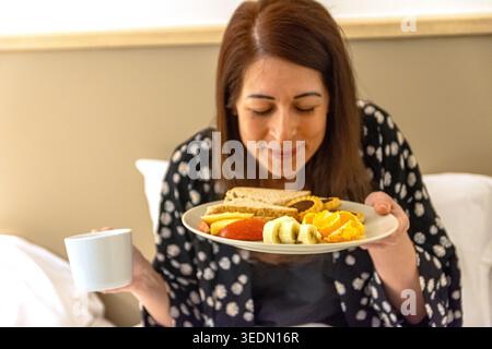 Frau genießt Frühstück im Bett während der morgendlichen Routine Stockfoto