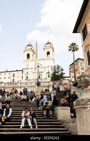 Menschen sitzen auf der Spanischen Treppe auf der Piazza di Spagna mit der Renaissance-Kirche Trinità dei Monti auf der Spitze in Rom, Italien. Stockfoto