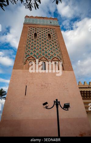 Das hohe Minarett der Kasbah-Moschee erhebt sich vor einem blauen Himmel in Marrakesch, Marokko, mit kunstvollen geometrischen Fliesen, ockerfarbener Backsteinarchitektur und Stockfoto