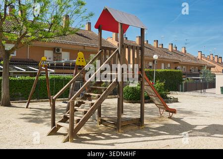 Leerer Kinderspielplatz mit Holzkletterstruktur, Rutsche und Schaukel in einer Wohngegend an einem sonnigen Tag. Öffentlicher Spielbereich im Freien. Stockfoto