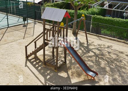 Leerer Kinderspielplatz mit Holzkletterstruktur, Rutsche und Schaukel in einer Wohngegend an einem sonnigen Tag. Öffentlicher Spielbereich im Freien. Stockfoto