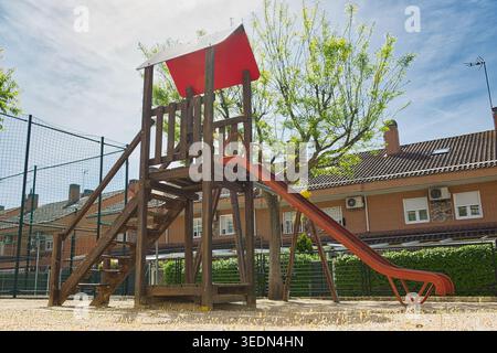 Leerer Kinderspielplatz mit Holzkletterstruktur, Rutsche und Schaukel in einer Wohngegend an einem sonnigen Tag. Öffentlicher Spielbereich im Freien. Stockfoto