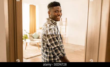 Ein junger Mann steht tagsüber in einem hellen Wohnzimmer in der Tür und lächelt Stockfoto