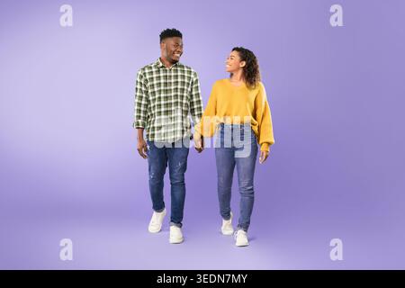 Ein Paar geht Hand in Hand auf einem violetten Hintergrund während eines verspielten Moments zusammen Stockfoto