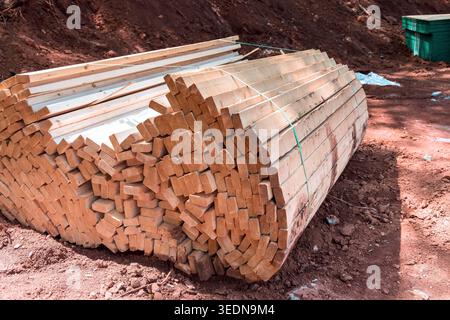Holzbalken werden ordentlich auf dem Boden auf der von Bäumen umgebenen Baustelle gestapelt Stockfoto