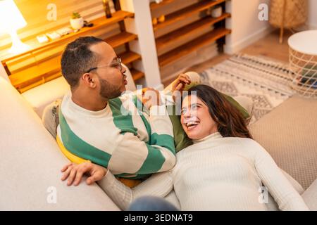 Junges Paar, das sich auf dem Sofa entspannt und sich zu Hause lacht Stockfoto
