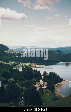 Malerische Seenlandschaft mit bewaldeten Hügeln, einem kleinen Dorf und einer gewundenen Straße, aus der Vogelperspektive auf die friedliche Landschaft mit Wasser und Bergen bei sanften Tagen Stockfoto