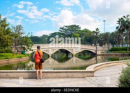 Eine Person steht auf einem Steindamm und blickt auf eine Bogenbrücke über einen Teich in einem Stadtpark. Outdoor-Erholung, städtische Landschaft, Brückenarchitektur Stockfoto