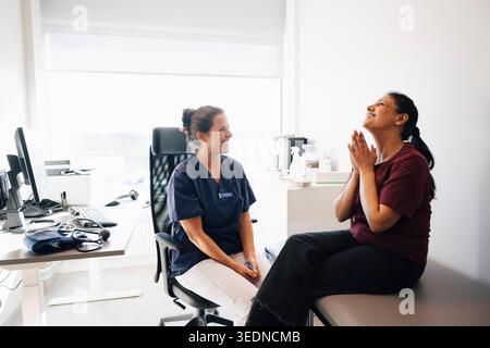 Glückliche weibliche Gesundheitsfachkraft, die in der Nähe der Frau sitzt und Dankbarkeit zeigt, nachdem sie gute Nachrichten im Krankenhaus gehört hat Stockfoto