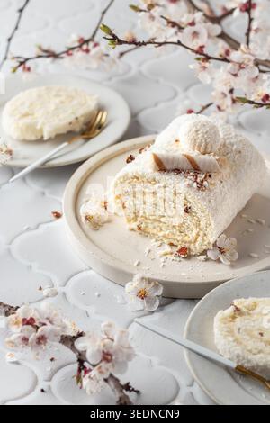 Geschnittener Kokos-Biskuit schweizer Brötchen auf weißem Fliesenhintergrund mit Frühlingsblumen Stockfoto