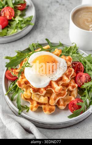 Herzhafte Waffeln mit Spiegelei und frischem Gemüse, serviert mit Kaffee auf grauem Hintergrund. Gesundes vegetarisches Frühstück Stockfoto