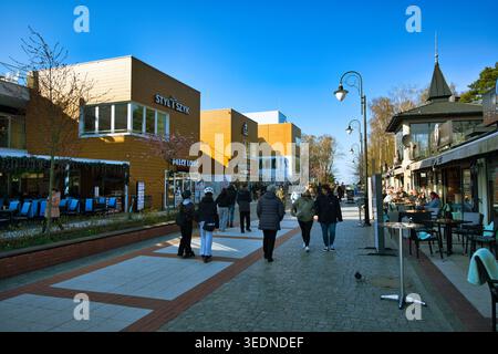 Menschen, die entlang der sonnigen Küstenpromenade mit Geschäften, Cafés und Restaurants am Wasser spazieren - die Küstenstadt Świnoujście. Stockfoto