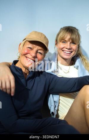 Porträt einer lächelnden Frau, die mit Arm um die ältere Mutter sitzt, vor farbigem Hintergrund Stockfoto