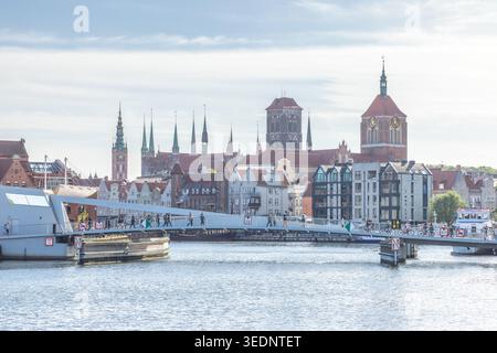 Danzig, Polen - 3. Mai 2025: Blick auf die Stadt mit einer modernen Fußgängerbrücke über den Fluss Motlawa mit historischen Gebäuden im Hintergrund. Stockfoto