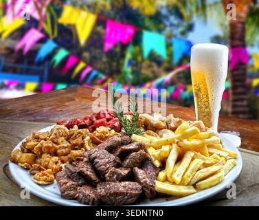 Eine köstliche brasilianische Snackplatte mit Rindfleisch, knusprigen Schweineschalen, Wurst, Huhn und Pommes frites, serviert mit einem kalten Bier gegen eine festliche Festa Stockfoto