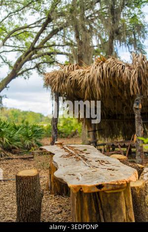 Rustikaler Picknicktisch im Freien aus roher Holzplatte und Baumstümpfen in der Nähe einer traditionellen Strohdachhütte auf einem Bauernhof. Stockfoto