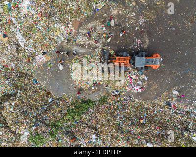 Aminbazar, Bangladesch - 26. Januar 2025: Luftaufnahme der Aminbazar-Deponie mit einem orangen Bulldozer, der Kunststoffabfälle und Abfallsammler transportiert Stockfoto
