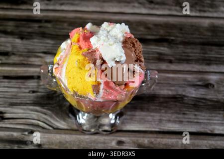 Ein Eisbecher mit verschiedenen Geschmacksrichtungen, der in einem Glasbecher im Vintage-Stil serviert wird, bietet mehrere Kugeln mit verschiedenen Eissorten, wie Schokolade, St. Stockfoto