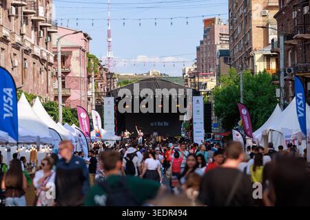 Beim Yerevan Wine Days Festival spazieren die Besucher am 7. Juni 2025 in Jerewan entlang einer überfüllten Festivalstraße, gesäumt von Verkostungszelten und einer Hauptbühne. Stockfoto