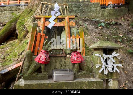 Fuchsstatuen mit roten Lätzchen und kupferfarbenen Torii-Toren am Fushimi Inari-Schrein, dem Haupt-Shinto-Schrein des Kami Inari Okami in Kyoto, Japan. Stockfoto