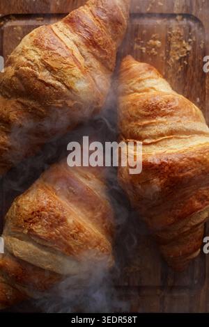 Frisch gebackene Buttercroissants mit Dampf auf Holzbrett Stockfoto
