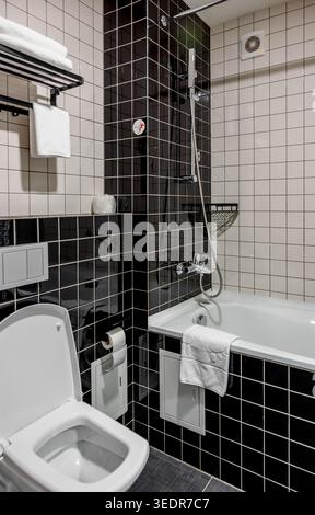 modernes Badezimmerinterieur mit weißer Badewannen-Dusche und gefliesten Wänden, sauberer Wohnraum mit Handtüchern und Duschvorhang in einem zeitgemäßen Raum Stockfoto