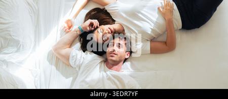 Ein glückliches junges Paar entspannt sich im Bett, lächelt und schaut sich an, während es einen zarten, intimen Moment in gemütlicher Atmosphäre während eines langsamen und faulen Wochenendes genießt Stockfoto