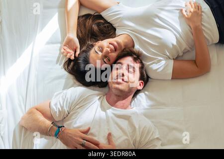 Ein junges Paar genießt einen faulen Wochenendmorgen im Bett, lächelt leise und hält sich fest, während es zu Hause Intimität, Vertrauen und ein warmes Gefühl der Zweisamkeit erlebt Stockfoto